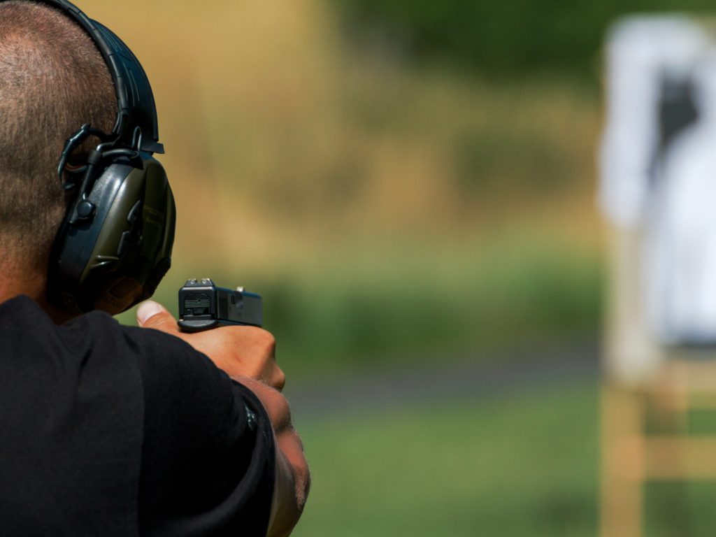 Shooter wearing ear protection aiming a handgun at a paper silhouette target during a live-fire range session, highlighting the use of dependable range day ammunition.