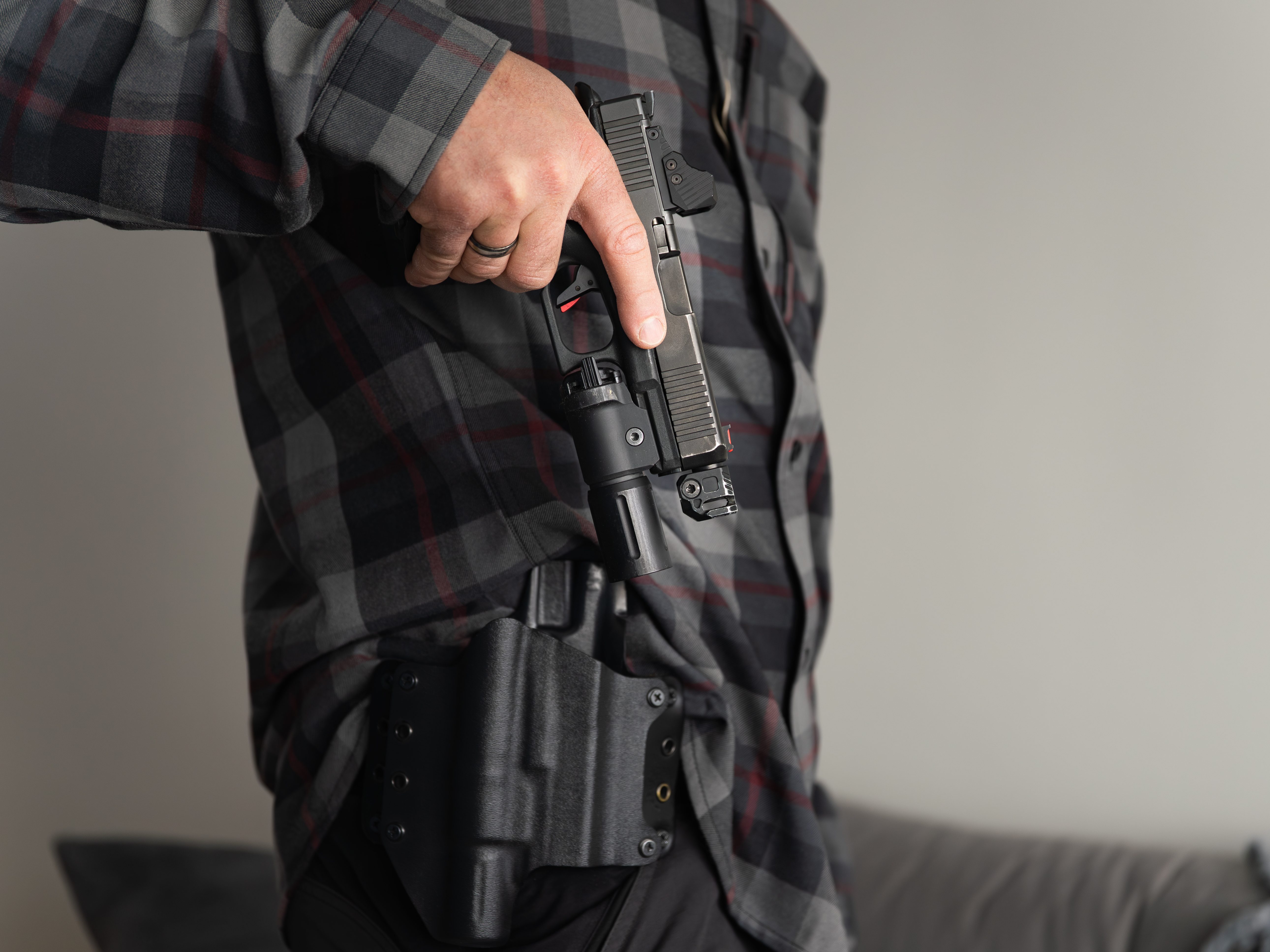 Person drawing a semi-automatic pistol from an inside-the-waistband holster while wearing a plaid shirt, illustrating concealed carry and personal defense readiness.